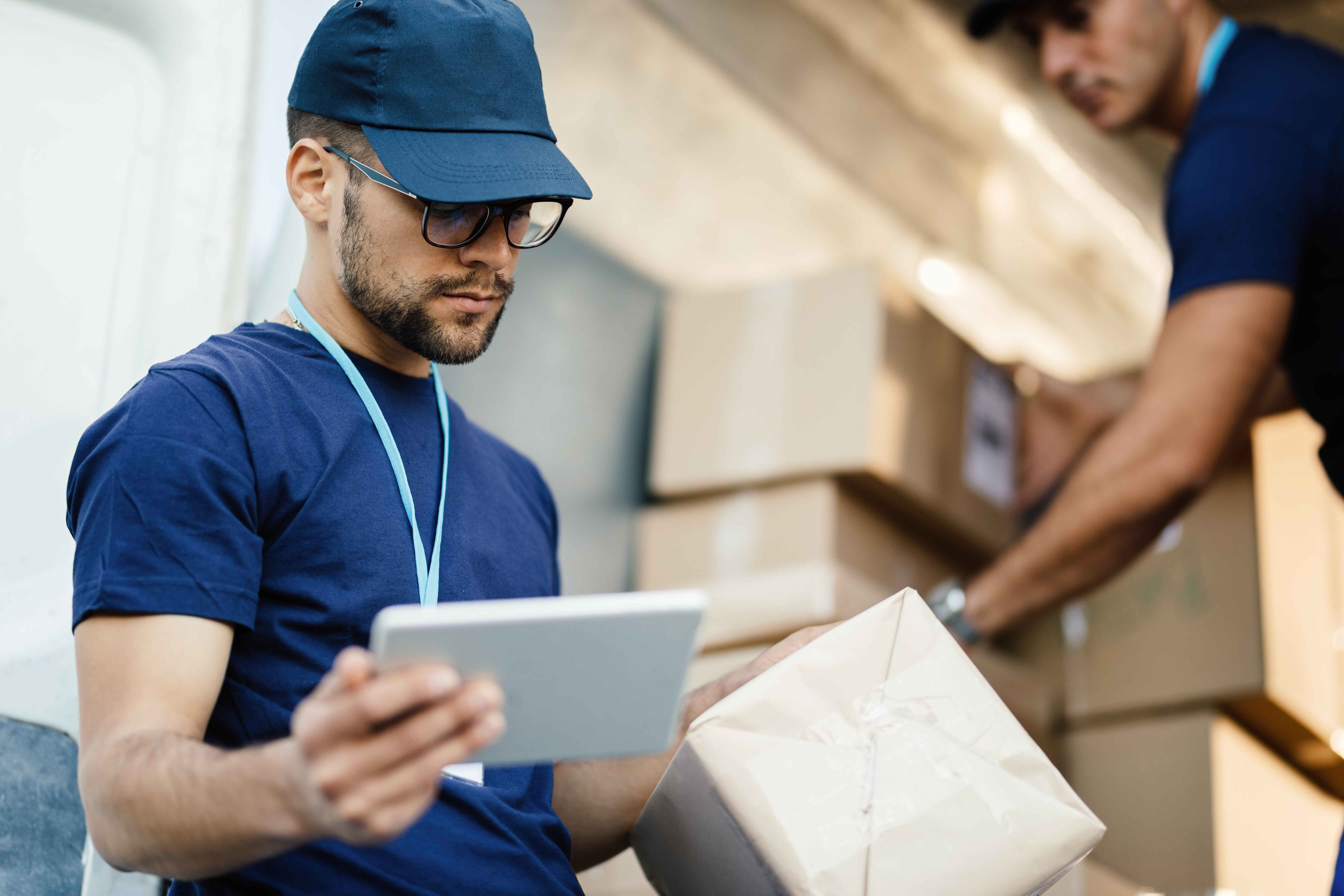 A man checking his tablet while holding a package 