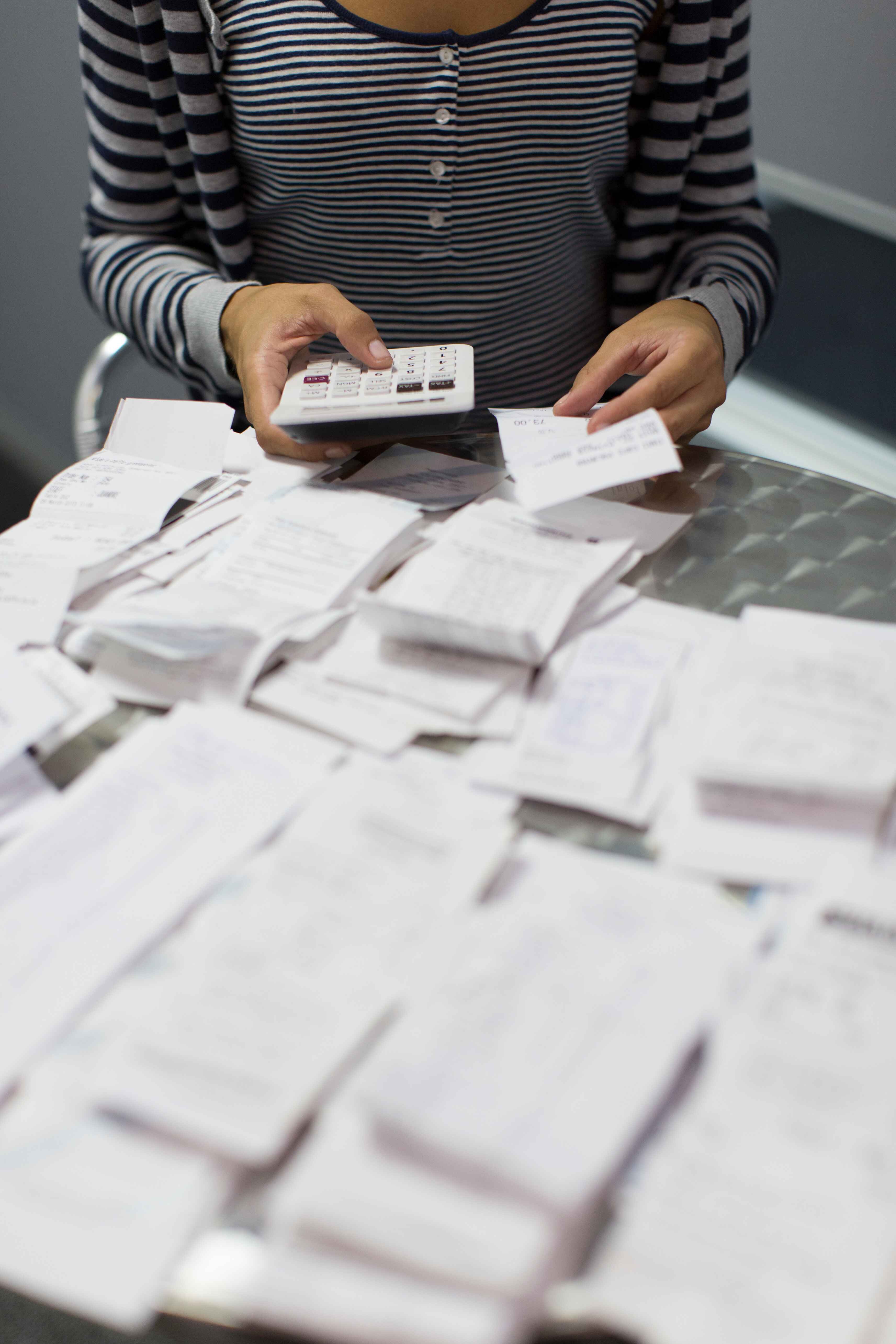 A woman with a calculator in one hand and a receipt in the other and a table full of receipts